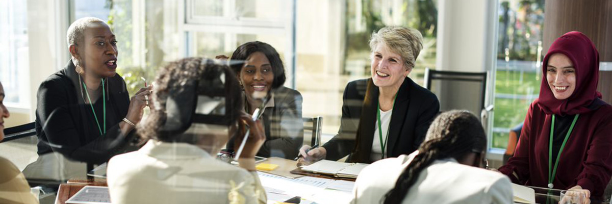 A group of diverse businesswomen are smiling or negotiating round an office table